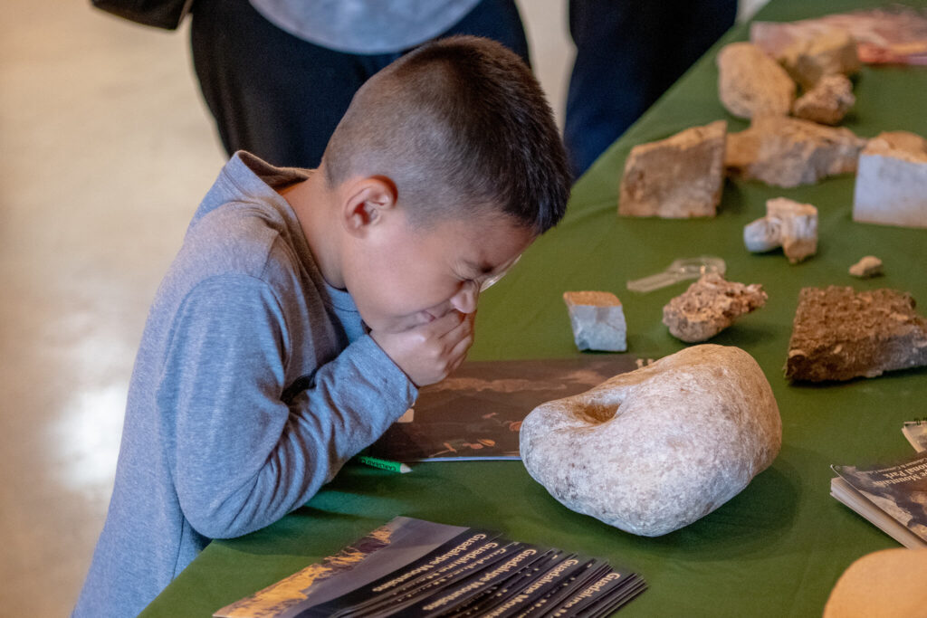 A child looking through a microscope to look closer at a rock formation of a cave in the NCKRI Cave Discovery Zone.