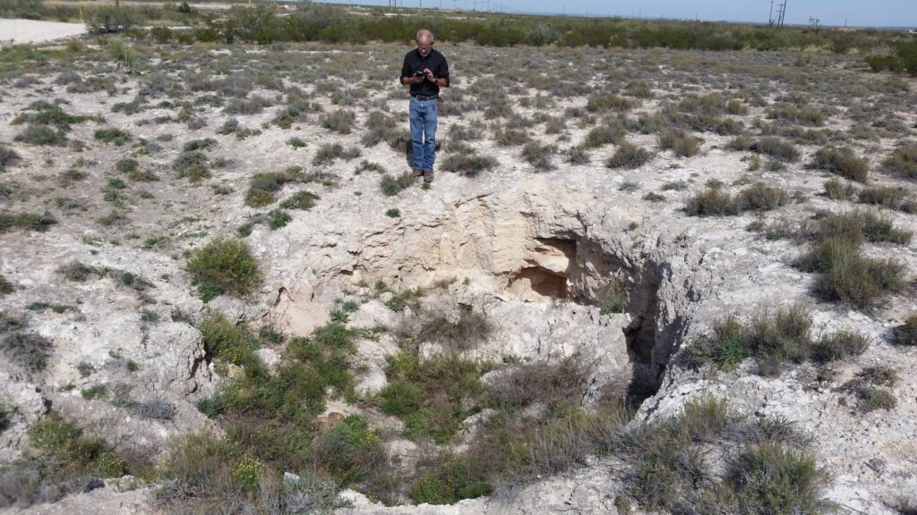 Sinkhole formed in gypsum bedrock about 100m east of U.S. Highway 285. Massive gypsum of the Rustler Formation exposed in the walls of the sinkhole.